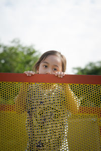 Portrait of a little girl with cute face holding fence and looking at the camera.