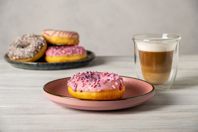 Glazed donuts on plates and coffee latte or cappuccino with milk foam in a heat-resistant glass cup. 