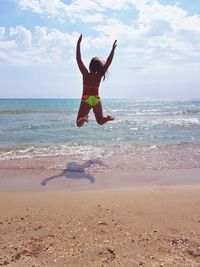 Rear view of young woman jumping at beach against sky