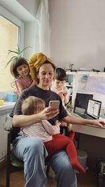Woman sitting at her home office with a laptop and a pink smartphone surrounded with three children