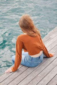 Rear view of woman sitting on pier over sea