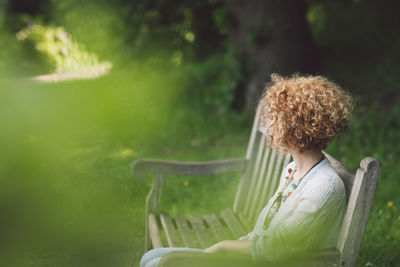 Side view of woman sitting on bench in park