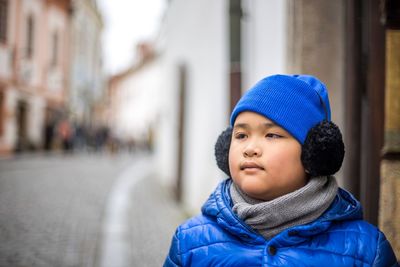 Boy in knit hat and ear muffs looking away by street