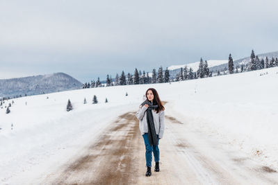 Woman walking on a road cover with snow while on a road trip in the mountains.