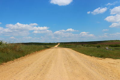 Dirt road amidst field against sky