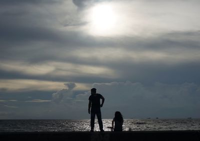 Rear view of father and son standing at beach during sunset