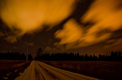 Road amidst silhouette trees against sky at night