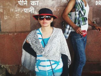 Young woman wearing sunglasses standing against wall