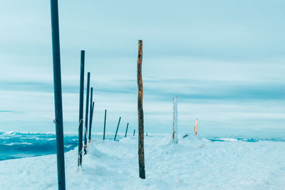 Wooden posts on snow covered field against sky