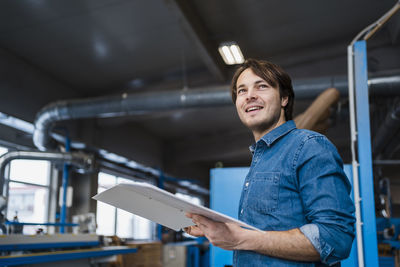 Male inspector with file smiling while standing at industry