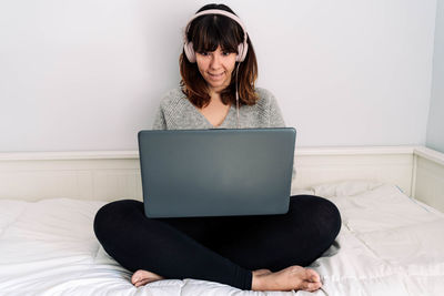 Young woman using phone while sitting on bed at home