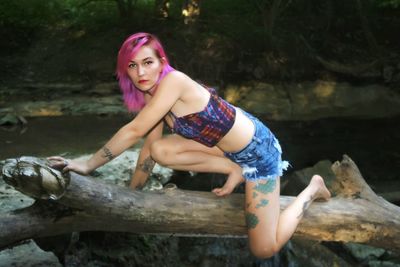 Portrait of seductive woman with dyed hair sitting on log