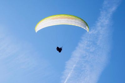 Low angle view of person paragliding against blue sky