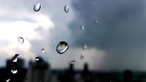 Close-up of wet glass window against sky during rainy season