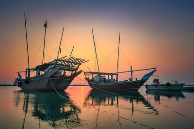 Fishing boats moored in sea against sky during sunset