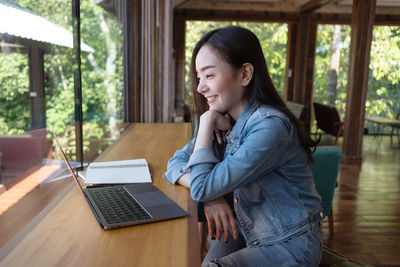 Side view of young woman using phone on table