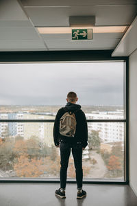 Rear view of man standing by window