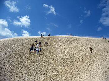 Low angle view of people standing at beach against blue sky