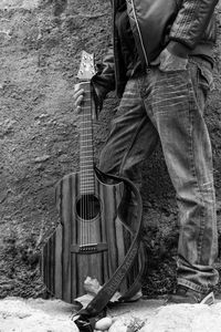 Low section of man standing with guitar against wall