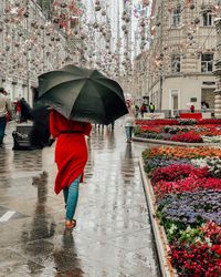 Low section of woman walking with umbrella on wet street during rainy season in city