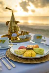 Close-up of dessert with tea cups on table against sea during sunset