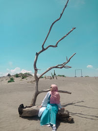 Woman sitting on land against blue sky