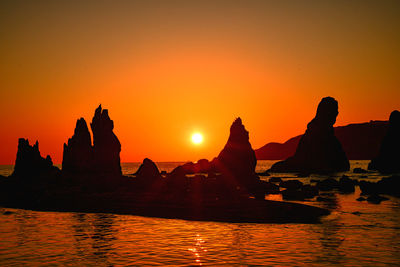 Silhouette rocks in sea against orange sky