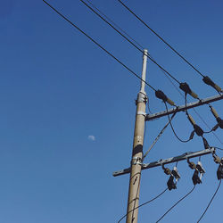 Low angle view of electricity pylon against clear blue sky