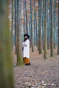 Man standing by tree trunk in forest