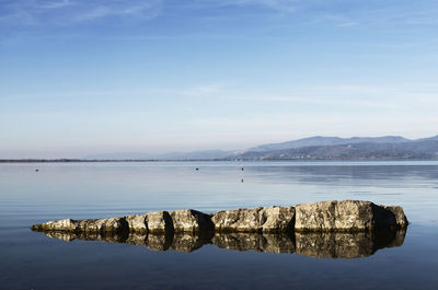 Rocks in the clear water of trasimeno lake in italy , in the background old small town
