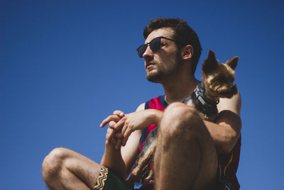 Low angle view of man with dog against clear blue sky