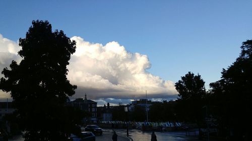 Silhouette trees leading towards city against blue sky