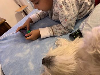 Side view of girl using mobile phone while lying by dog on bed at home