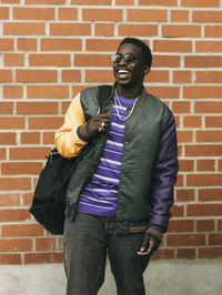 Happy young man with backpack while standing in front of brick wall