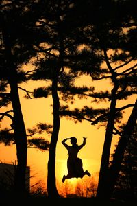 Silhouette woman jumping by trees against sky during sunset