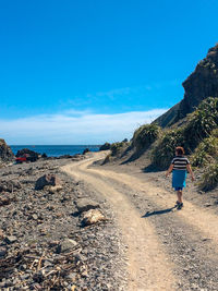 Rear view of woman walking on road against blue sky during sunny day