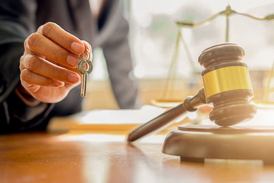 Midsection of man holding keys by gavel and sounding block on table