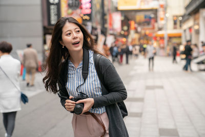 Young woman using phone while standing on street in city