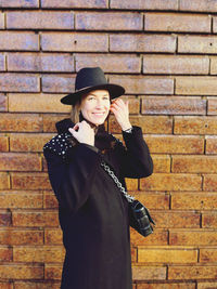 Young woman wearing hat standing against brick wall