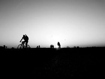 Silhouette people riding bicycle against clear sky