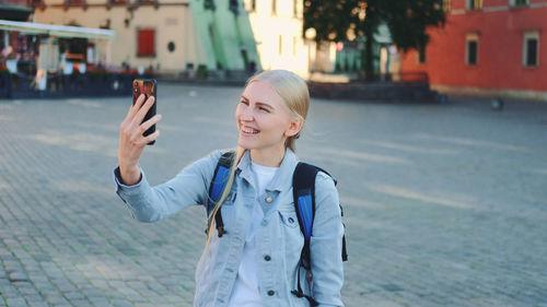 Young woman using phone while standing on street in city