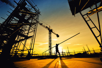 Silhouette man working at construction site against sky during sunset
