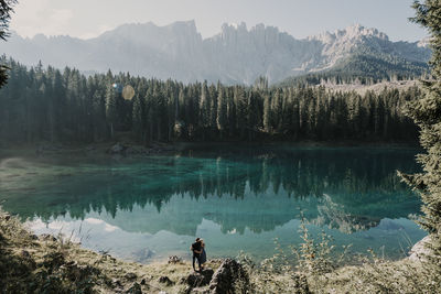 Man and woman standing on rock at carezza lake during sunny day in south tyrol, italy