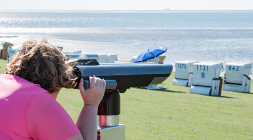 Woman looking at sea through binoculars on field