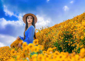 Young woman with yellow flowers against sky