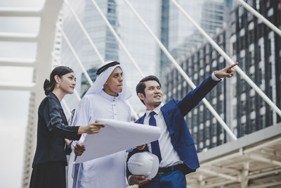 Business people looking at businessman pointing against metallic structure