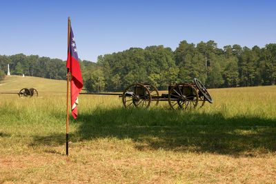 Cart and flag on grassy field against sky during sunny day