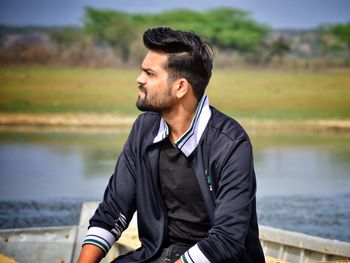Young man looking away while standing on lake