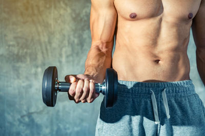 Midsection of shirtless man lifting dumbbell