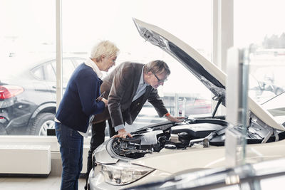 Senior couple examining car engine in showroom